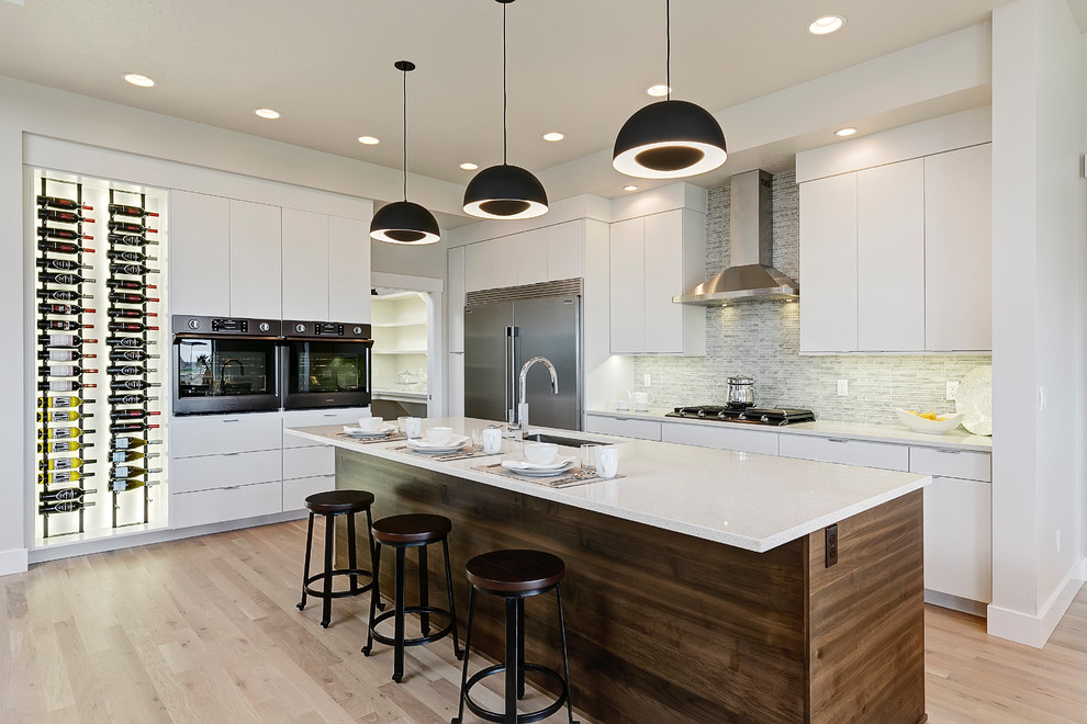 This is an example of a modern l-shaped kitchen in Boise with a submerged sink, flat-panel cabinets, white cabinets, grey splashback, stainless steel appliances, light hardwood flooring, an island, beige floors and white worktops.