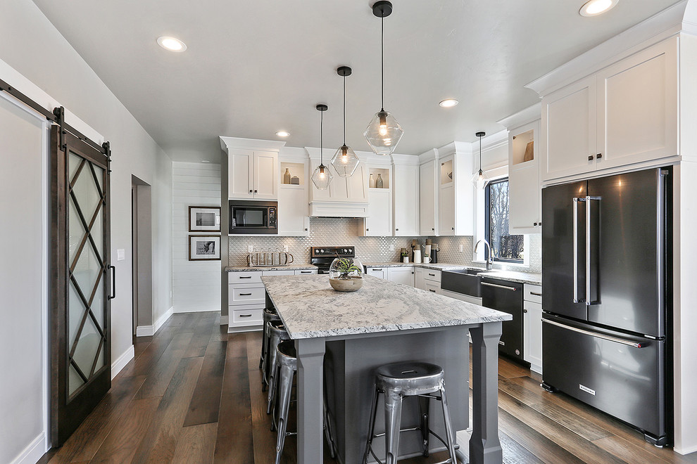 Example of a classic medium tone wood floor and brown floor eat-in kitchen design in Milwaukee with a farmhouse sink, flat-panel cabinets, white cabinets, quartz countertops, white backsplash, ceramic backsplash, black appliances and an island