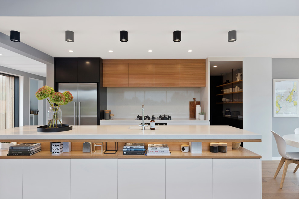 Zweizeilige Moderne Küche mit Unterbauwaschbecken, flächenbündigen Schrankfronten, weißen Schränken, Küchenrückwand in Weiß, Küchengeräten aus Edelstahl, hellem Holzboden, Kücheninsel, beigem Boden und weißer Arbeitsplatte in Wellington
