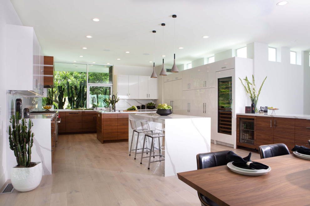 Modern inredning av ett stort vit vitt kök, med släta luckor, bänkskiva i kvarts, ljust trägolv, en undermonterad diskho, vita skåp, vitt stänkskydd, flera köksöar och beiget golv
