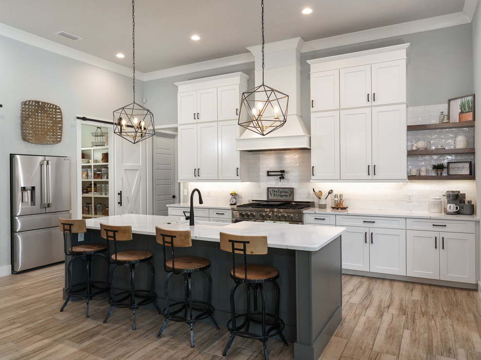 Inspiration for a large farmhouse single-wall porcelain tile and brown floor kitchen pantry remodel in Jacksonville with a farmhouse sink, shaker cabinets, white cabinets, quartz countertops, white backsplash, subway tile backsplash, stainless steel appliances, an island and white countertops