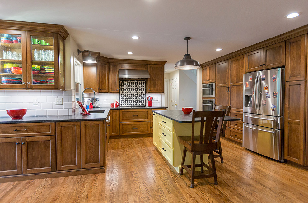 Inspiration for a mid-sized timeless u-shaped medium tone wood floor open concept kitchen remodel in Cincinnati with an undermount sink, shaker cabinets, white backsplash, ceramic backsplash, stainless steel appliances, an island, medium tone wood cabinets, granite countertops and black countertops
