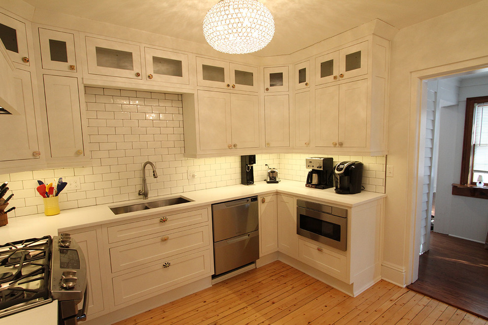 Inredning av ett klassiskt mellanstort vit vitt kök, med en undermonterad diskho, luckor med infälld panel, vita skåp, vitt stänkskydd, rostfria vitvaror och ljust trägolv