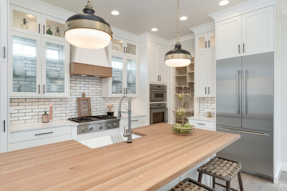 Inspiration for a mid-sized country u-shaped light wood floor and beige floor eat-in kitchen remodel in Boise with a farmhouse sink, recessed-panel cabinets, white cabinets, quartzite countertops, white backsplash, subway tile backsplash, stainless steel appliances, an island and white countertops