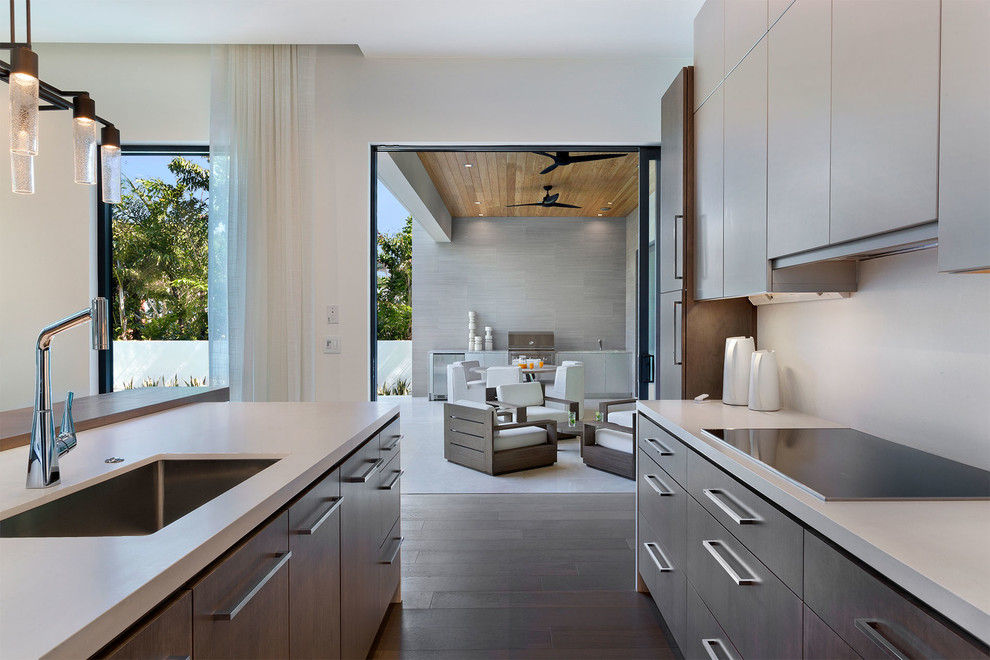 Inspiration for a huge modern single-wall medium tone wood floor and brown floor open concept kitchen remodel in Miami with an undermount sink, flat-panel cabinets, white cabinets, solid surface countertops, beige backsplash, black appliances, an island and beige countertops