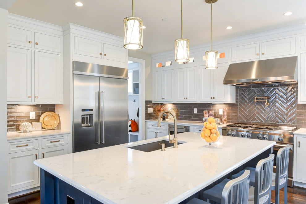 Inspiration for a large transitional l-shaped medium tone wood floor and brown floor kitchen remodel in Baltimore with an undermount sink, shaker cabinets, white cabinets, gray backsplash, glass tile backsplash, stainless steel appliances, an island and white countertops