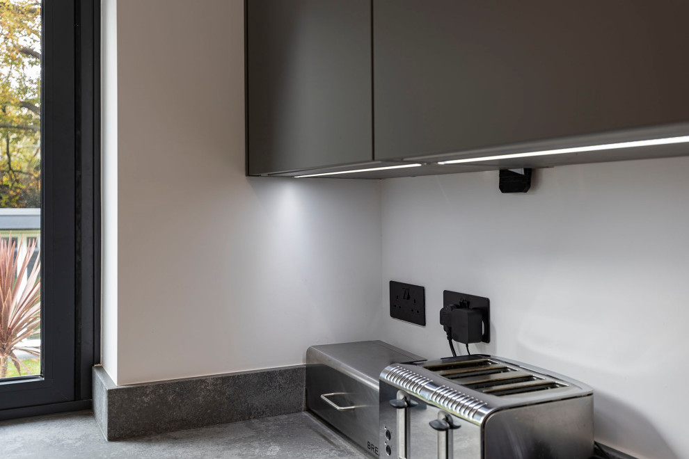 This is an example of a medium sized modern u-shaped kitchen in Hertfordshire with a built-in sink, recessed-panel cabinets, concrete worktops, grey splashback, granite splashback, stainless steel appliances, laminate floors and grey worktops.