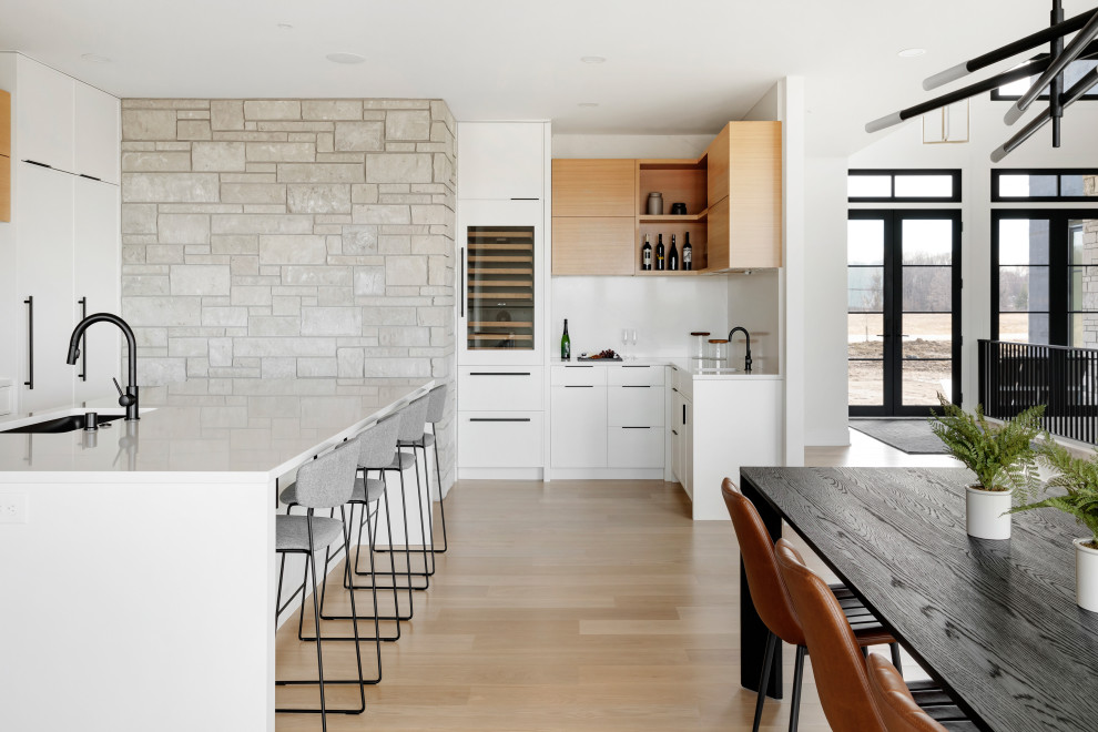 Cette image montre une cuisine design avec des portes de placard blanches, un plan de travail en quartz, un électroménager en acier inoxydable, parquet clair, îlot, un sol marron et un plan de travail blanc.