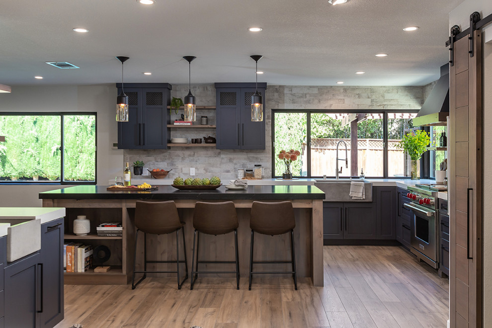 Idéer för att renovera ett mellanstort industriellt linjärt kök med öppen planlösning, med en rustik diskho, luckor med infälld panel, blå skåp, granitbänkskiva, grått stänkskydd, stänkskydd i keramik, rostfria vitvaror, vinylgolv, en köksö och brunt golv