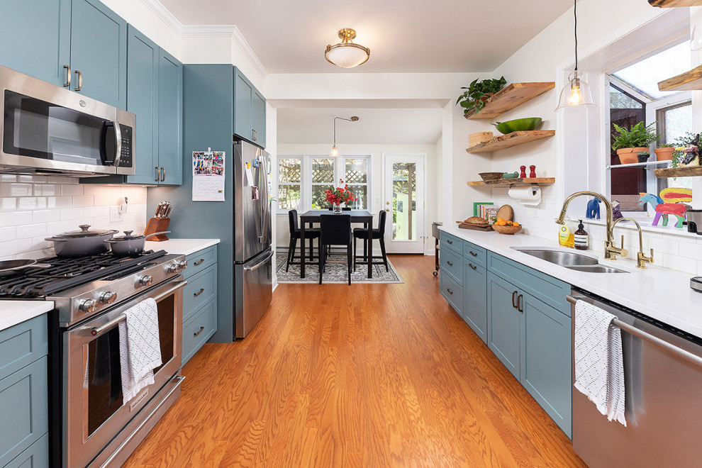 Exempel på ett mellanstort vit vitt kök, med en undermonterad diskho, skåp i shakerstil, blå skåp, bänkskiva i kvarts, vitt stänkskydd, stänkskydd i tunnelbanekakel, rostfria vitvaror, mellanmörkt trägolv och brunt golv