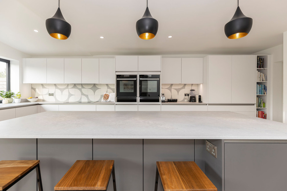 Idéer för att renovera ett stort minimalistiskt grå grått kök med öppen planlösning, med en nedsänkt diskho, luckor med infälld panel, granitbänkskiva, stänkskydd i mosaik, svarta vitvaror, laminatgolv, en köksö och beiget golv