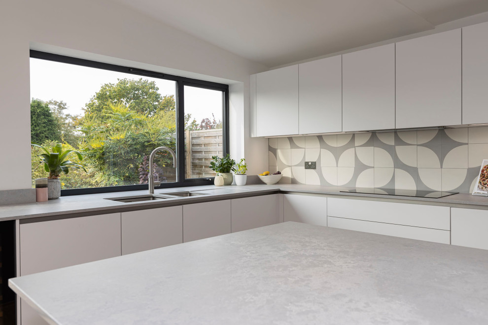 Bild på ett stort skandinaviskt grå grått kök med öppen planlösning, med en nedsänkt diskho, luckor med infälld panel, granitbänkskiva, stänkskydd i mosaik, svarta vitvaror, laminatgolv, en köksö och beiget golv