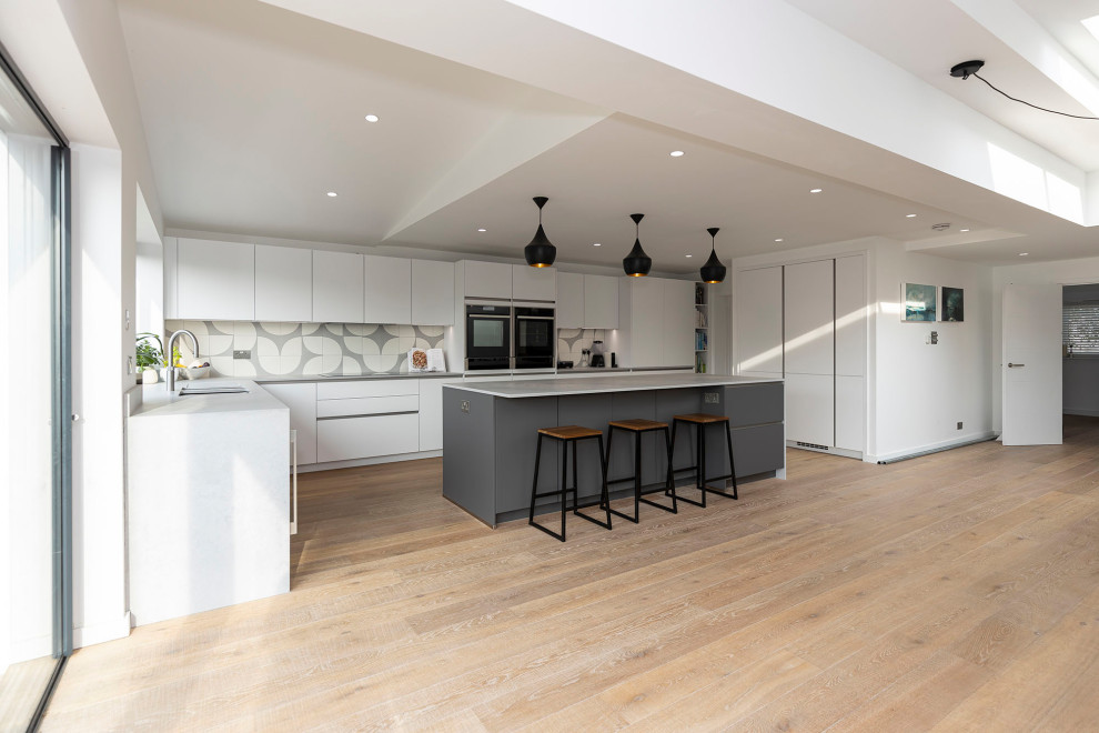 Nordisk inredning av ett stort grå grått kök med öppen planlösning, med en nedsänkt diskho, luckor med infälld panel, granitbänkskiva, stänkskydd i mosaik, svarta vitvaror, laminatgolv, en köksö och beiget golv