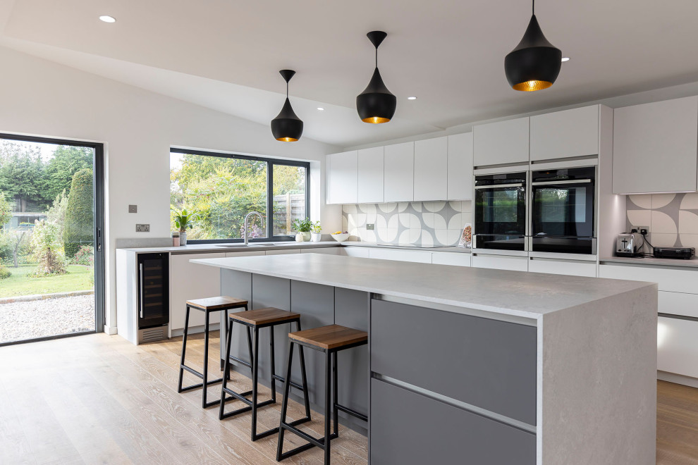 Inspiration för ett stort minimalistiskt grå grått kök med öppen planlösning, med en nedsänkt diskho, luckor med infälld panel, granitbänkskiva, stänkskydd i mosaik, svarta vitvaror, laminatgolv, en köksö och beiget golv