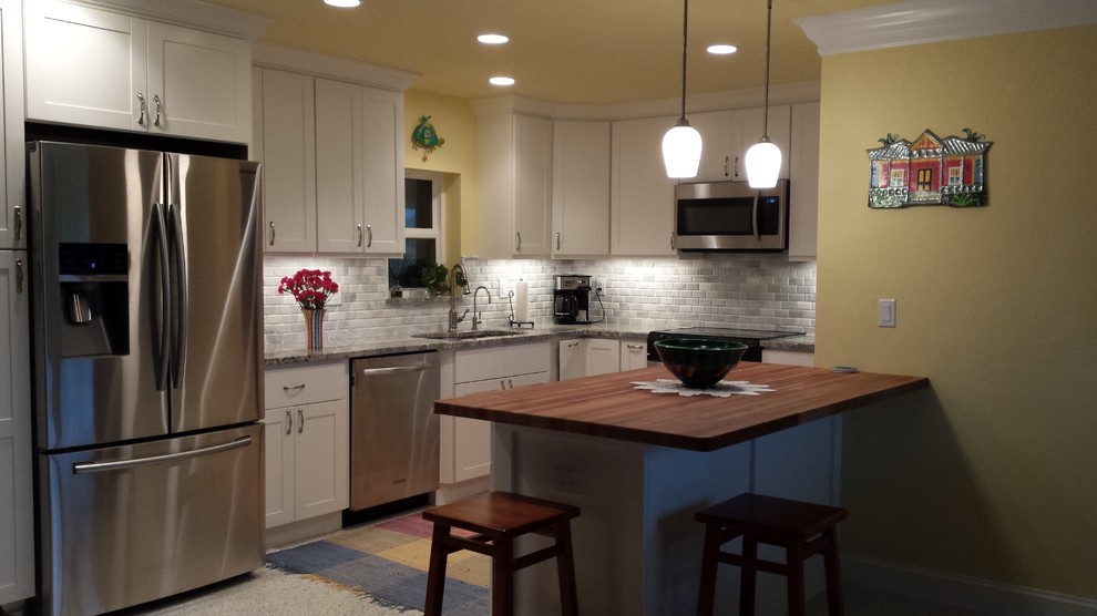 Foto på ett litet maritimt kök, med en undermonterad diskho, vita skåp, vitt stänkskydd, stänkskydd i stenkakel, rostfria vitvaror, skåp i shakerstil, träbänkskiva och terrazzogolv