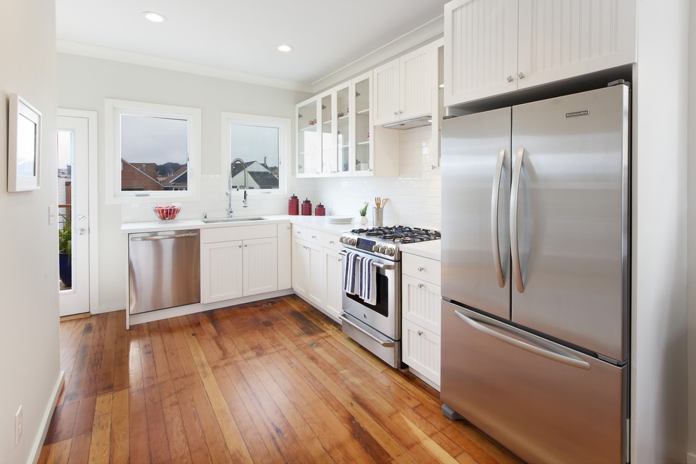 Mid-sized elegant single-wall medium tone wood floor and brown floor open concept kitchen photo in San Francisco with shaker cabinets, white cabinets, quartz countertops, white backsplash, subway tile backsplash, stainless steel appliances, no island and an undermount sink