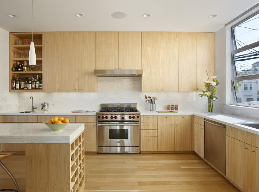 Imagen de cocina actual con armarios con paneles lisos, puertas de armario de madera clara, salpicadero blanco y electrodomésticos de acero inoxidable