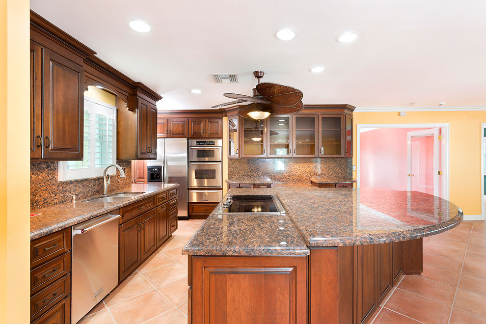 Expansive beach style l-shaped kitchen/diner in Miami with a built-in sink, raised-panel cabinets, medium wood cabinets, granite worktops, multi-coloured splashback, stainless steel appliances, terracotta flooring, an island, pink floors and multicoloured worktops.