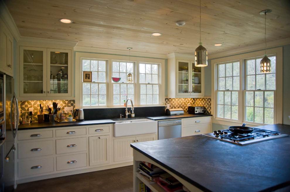 Bild på ett stort lantligt kök, med en rustik diskho, skåp i shakerstil, vita skåp, bänkskiva i täljsten, grönt stänkskydd, stänkskydd i keramik, rostfria vitvaror, betonggolv och en köksö