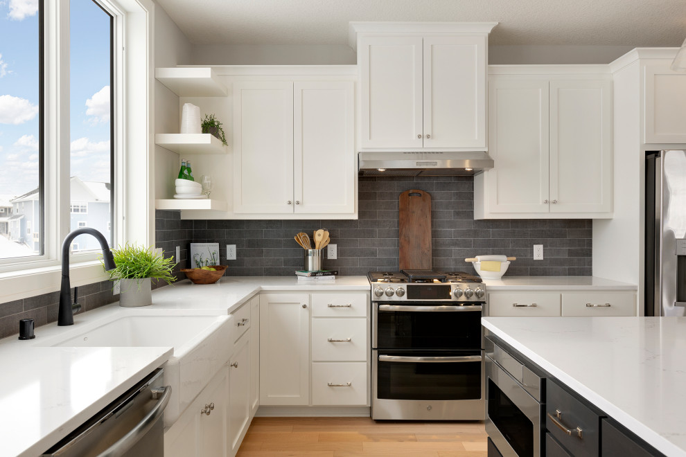 Exempel på ett klassiskt vit vitt l-kök, med en rustik diskho, skåp i shakerstil, vita skåp, bänkskiva i kvartsit, grått stänkskydd, stänkskydd i tunnelbanekakel, rostfria vitvaror, ljust trägolv och en köksö