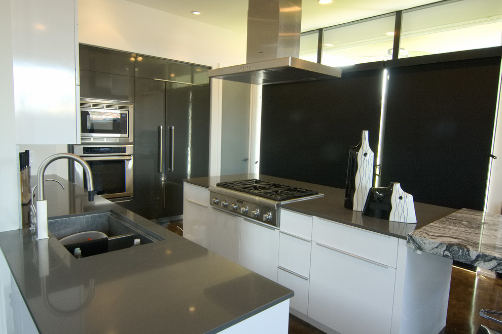 This is an example of a large modern u-shaped kitchen/diner with a double-bowl sink, flat-panel cabinets, white cabinets, granite worktops, grey splashback, mosaic tiled splashback, coloured appliances, concrete flooring, an island, brown floors and grey worktops.