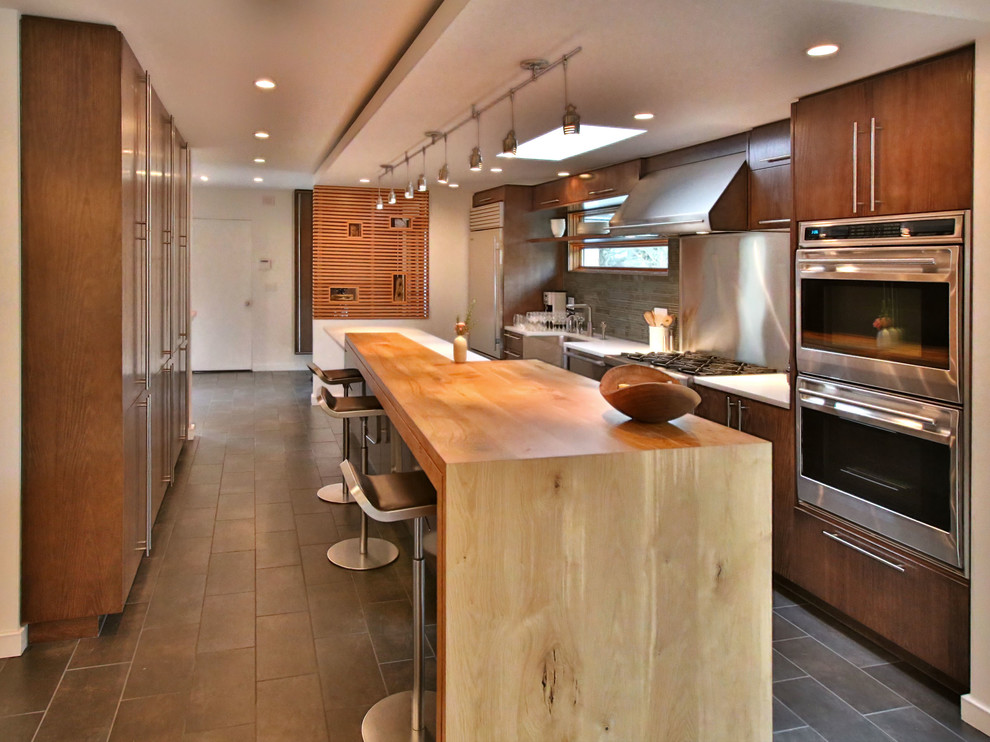 Cette image montre une cuisine américaine design en bois foncé avec un évier de ferme, un placard à porte shaker, un plan de travail en bois, une crédence en dalle métallique et un électroménager en acier inoxydable.
