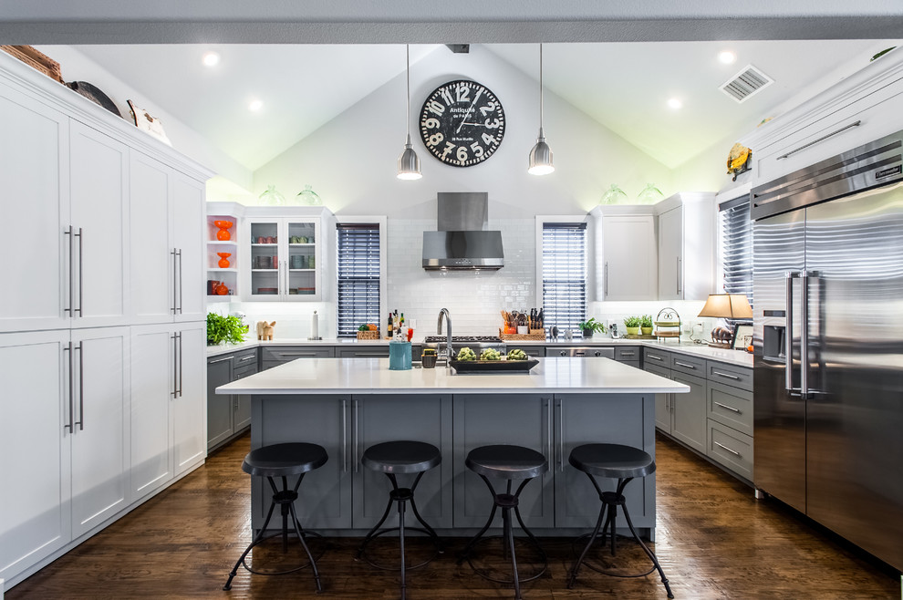 Klassische Küche in grau-weiß mit Schrankfronten im Shaker-Stil, grauen Schränken, Küchenrückwand in Weiß, Küchengeräten aus Edelstahl, braunem Holzboden und Kücheninsel in Dallas