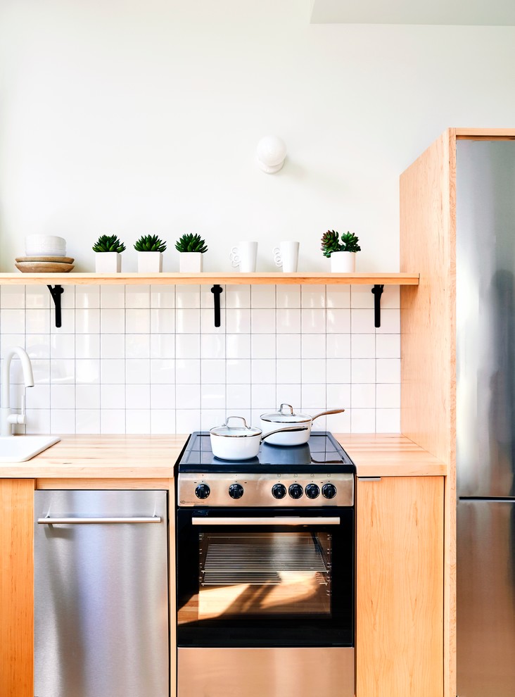 プロビデンスにある小さな北欧スタイルのおしゃれなキッチン (ドロップインシンク、フラットパネル扉のキャビネット、淡色木目調キャビネット、木材カウンター、白いキッチンパネル、磁器タイルのキッチンパネル、シルバーの調理設備、淡色無垢フローリング、アイランドなし、ベージュの床) の写真
