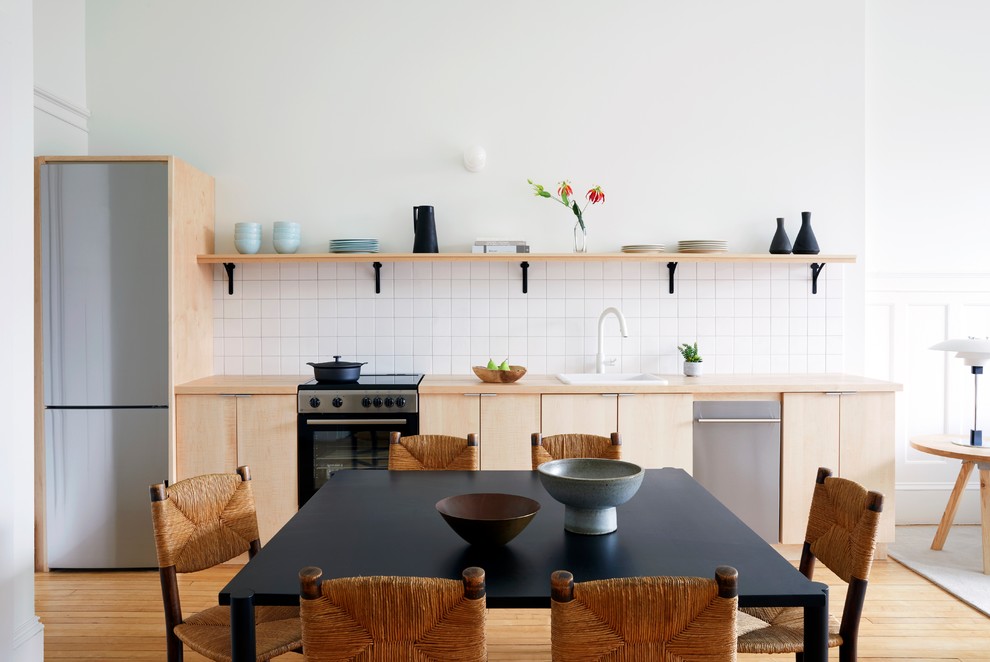 Inspiration for a scandi single-wall open plan kitchen in Providence with a built-in sink, flat-panel cabinets, light wood cabinets, wood worktops, white splashback, porcelain splashback, stainless steel appliances, light hardwood flooring, no island and beige floors.
