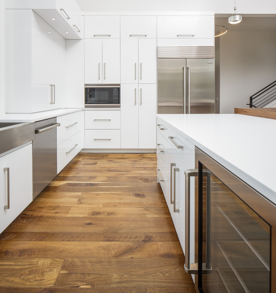 This is an example of a contemporary kitchen/diner in Denver with a belfast sink, white cabinets, stainless steel appliances, medium hardwood flooring and an island.