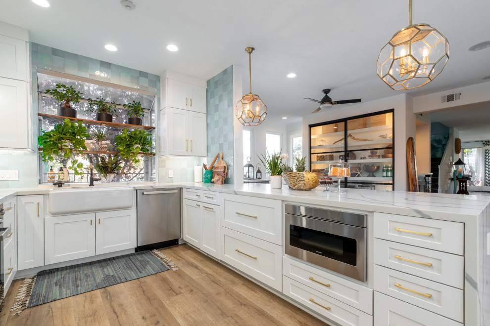 This is an example of a large rural u-shaped kitchen in Orange County with a belfast sink, recessed-panel cabinets, white cabinets, engineered stone countertops, blue splashback, ceramic splashback, stainless steel appliances, laminate floors, multi-coloured floors and white worktops.