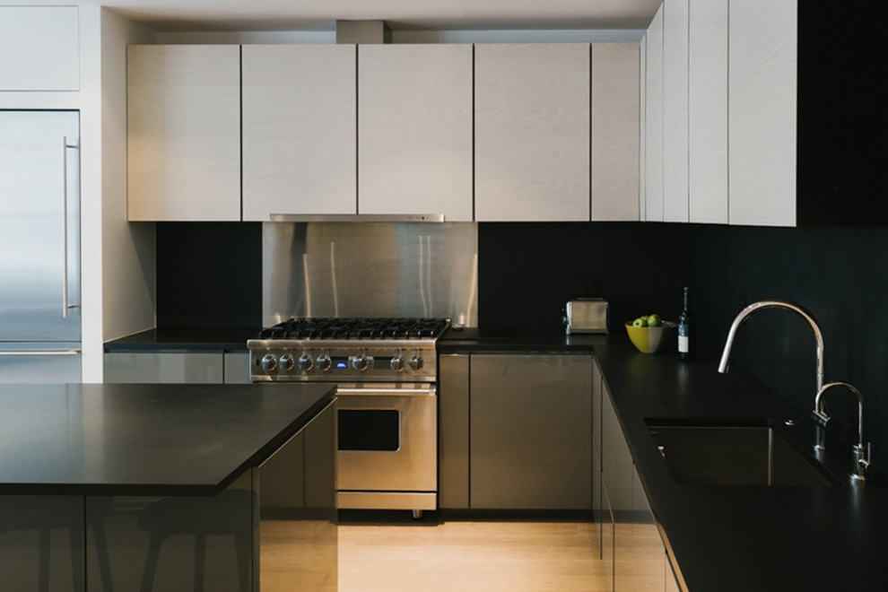 Large contemporary u-shaped kitchen/diner in New York with flat-panel cabinets, light wood cabinets, black splashback, stainless steel appliances, light hardwood flooring and an island.