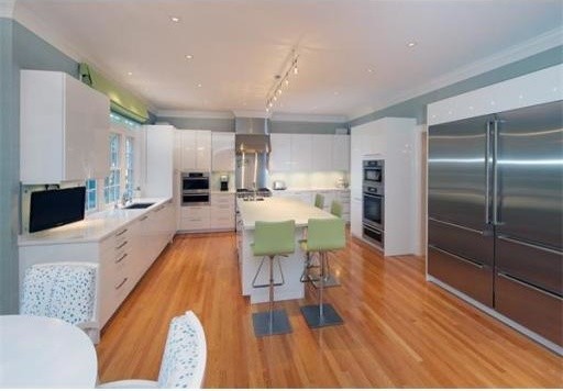 Inspiration for a large classic l-shaped kitchen/diner in Boston with a built-in sink, flat-panel cabinets, white cabinets, glass worktops, white splashback, stainless steel appliances, medium hardwood flooring and an island.