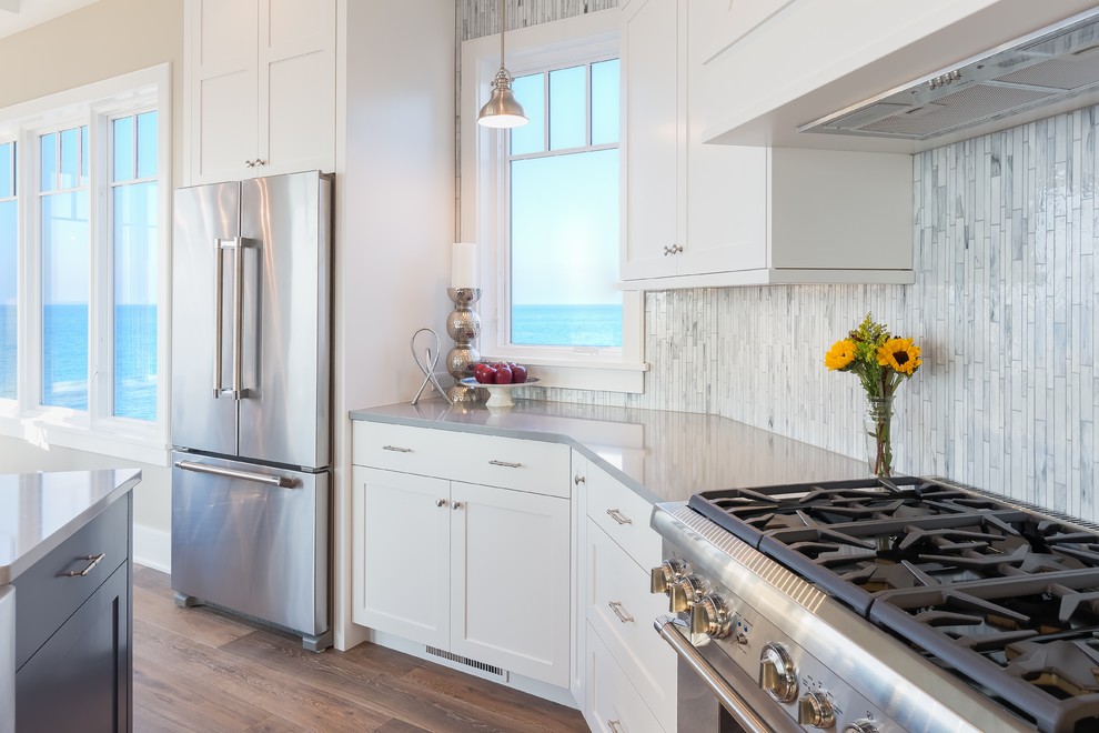 Photo of a beach style kitchen in Grand Rapids with shaker cabinets, white cabinets, blue splashback, matchstick tiled splashback, stainless steel appliances, medium hardwood flooring and an island.