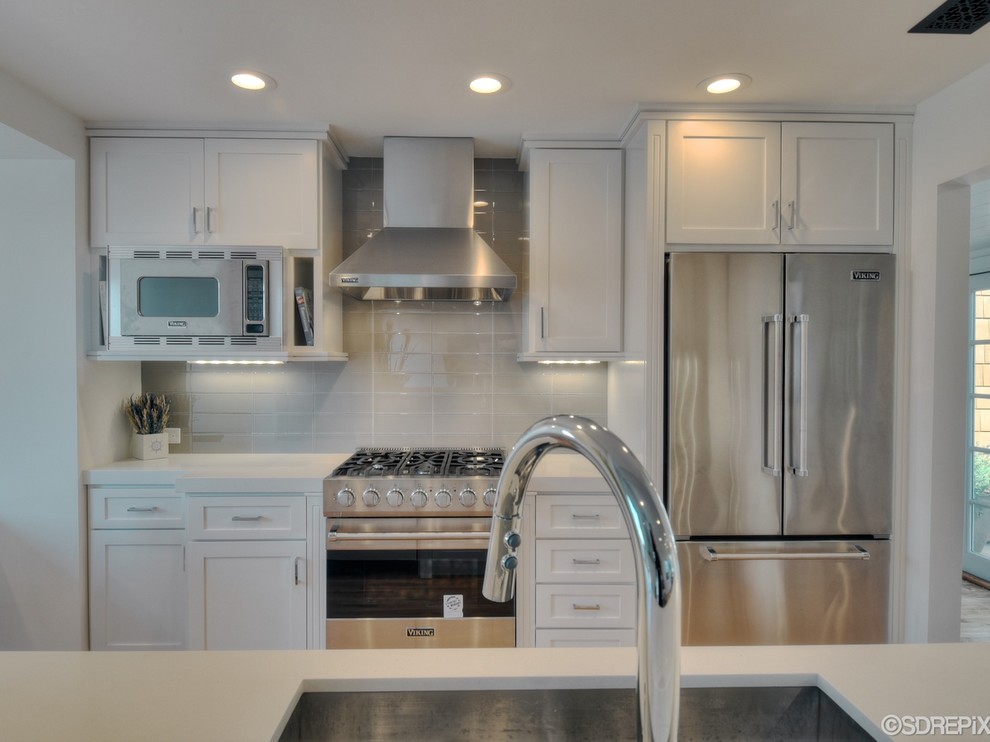Design ideas for a small nautical galley open plan kitchen in San Diego with a belfast sink, shaker cabinets, white cabinets, composite countertops, white splashback, glass tiled splashback, stainless steel appliances and light hardwood flooring.