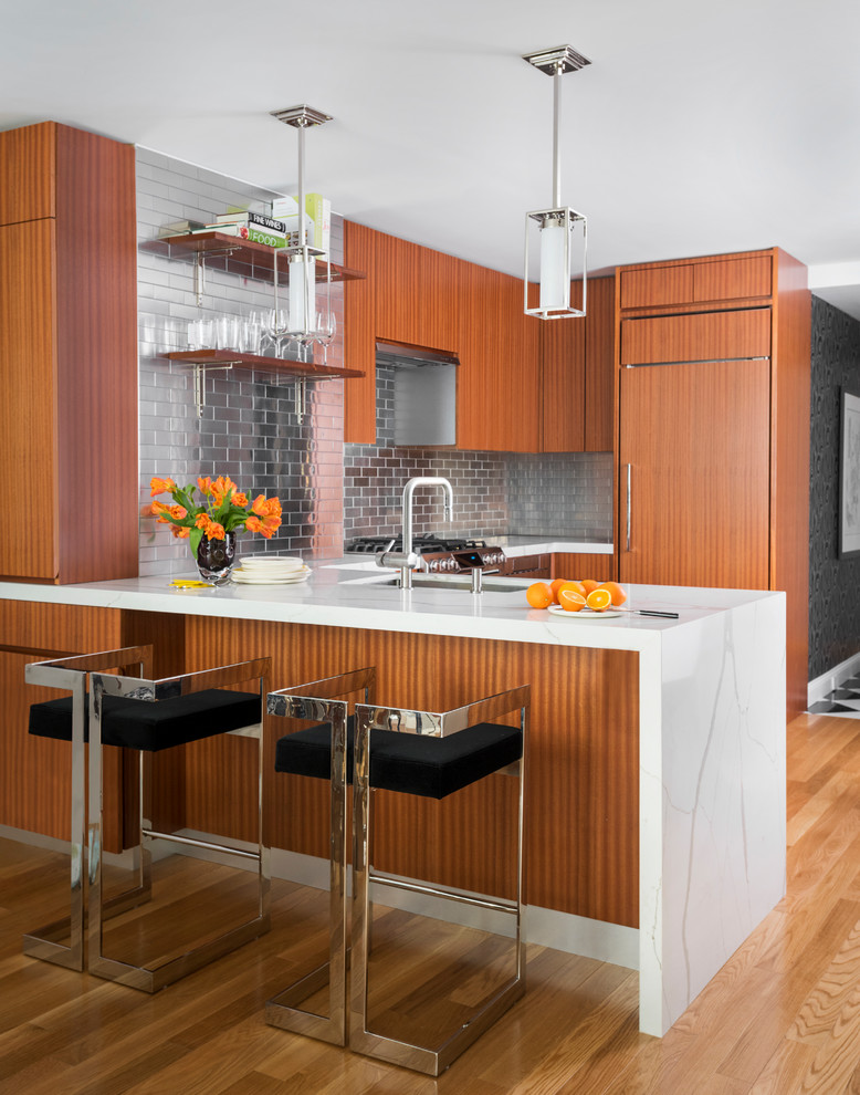 Foto på ett mellanstort funkis vit u-kök, med en undermonterad diskho, släta luckor, skåp i mellenmörkt trä, stänkskydd med metallisk yta, stänkskydd i metallkakel, integrerade vitvaror, ljust trägolv, en halv köksö, marmorbänkskiva och brunt golv