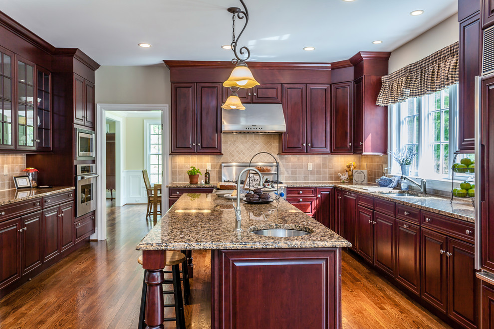 Enclosed kitchen - large transitional u-shaped laminate floor and brown floor enclosed kitchen idea in Bridgeport with an undermount sink, raised-panel cabinets, red cabinets, granite countertops, beige backsplash, stone tile backsplash, stainless steel appliances and an island