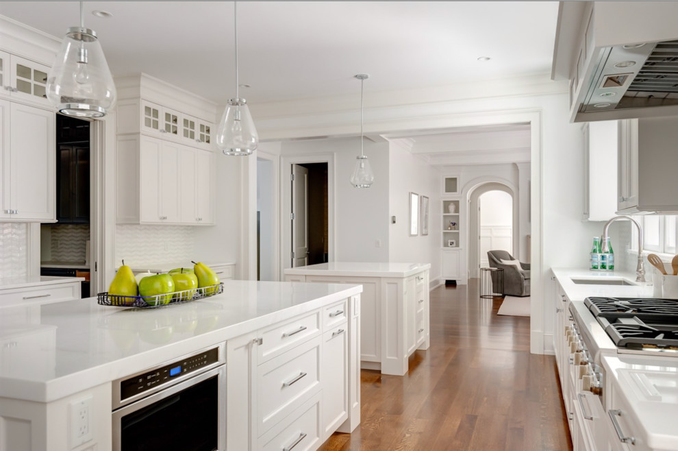 Design ideas for an expansive traditional u-shaped open plan kitchen in Boston with recessed-panel cabinets, white cabinets, composite countertops, white splashback, multiple islands and white worktops.