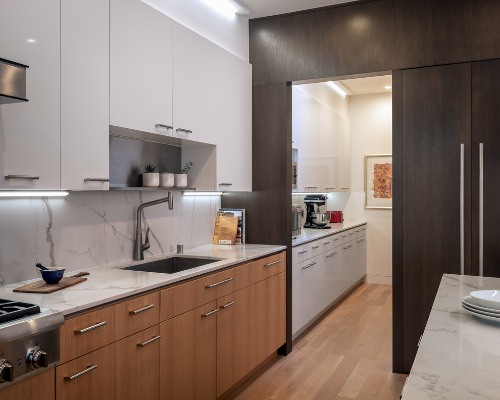 Inspiration for a large mid-century modern u-shaped medium tone wood floor open concept kitchen remodel in San Francisco with an undermount sink, flat-panel cabinets, white cabinets, marble countertops, white backsplash, stone slab backsplash, paneled appliances, an island and white countertops
