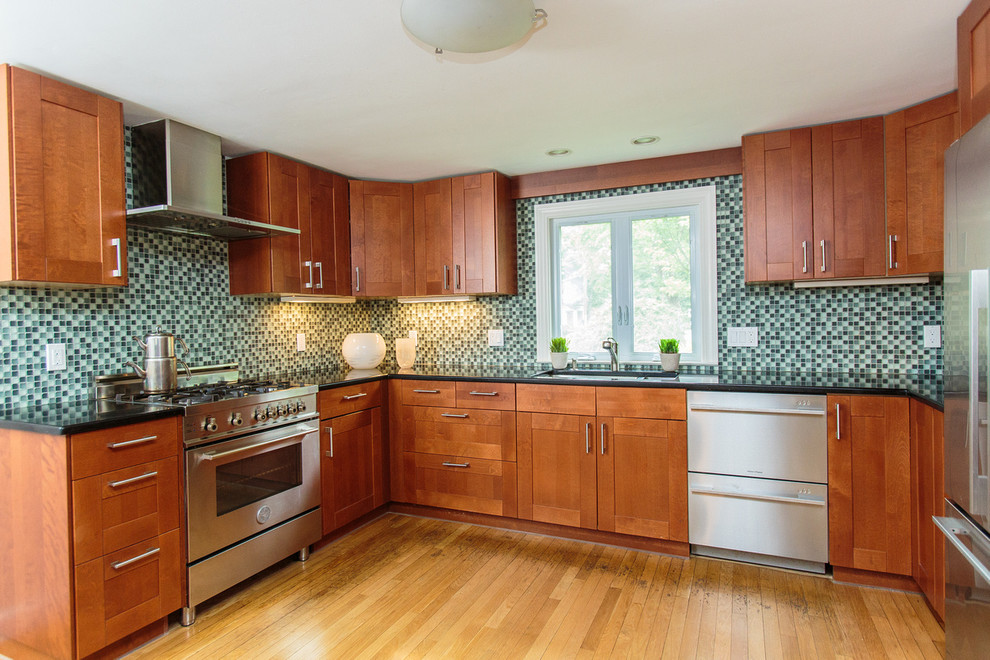 Large classic l-shaped open plan kitchen in Boston with a built-in sink, recessed-panel cabinets, medium wood cabinets, granite worktops, multi-coloured splashback, glass tiled splashback, stainless steel appliances, medium hardwood flooring and an island.