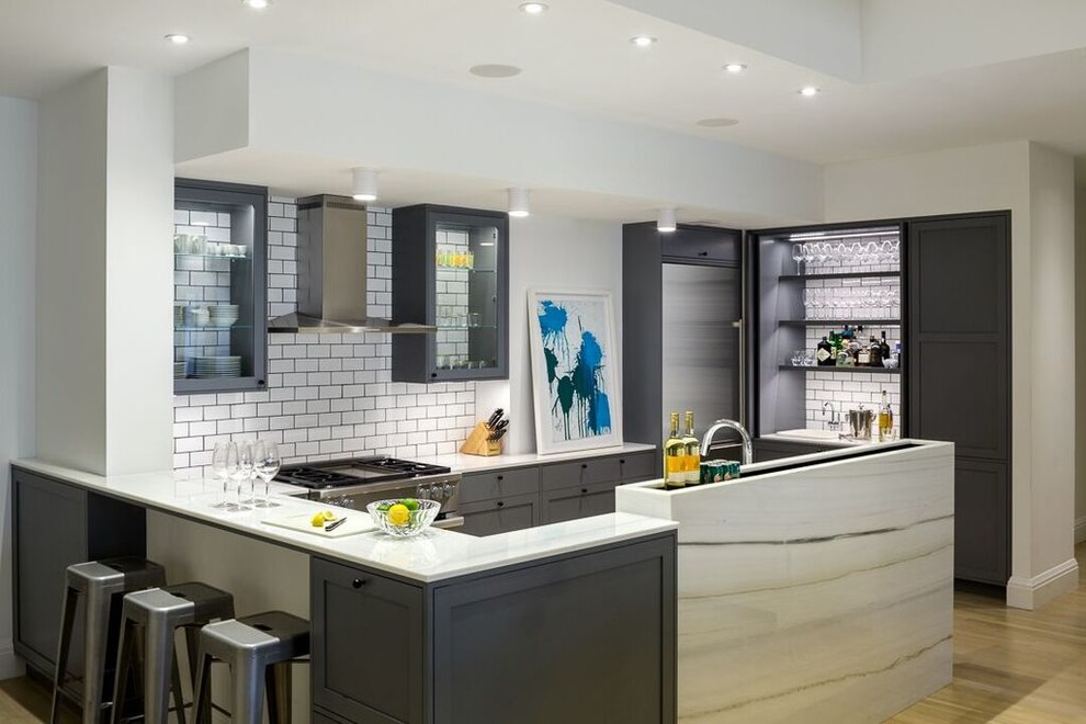 Traditional u-shaped kitchen in New York with glass-front cabinets, grey cabinets, white splashback, metro tiled splashback, stainless steel appliances, light hardwood flooring and beige floors.
