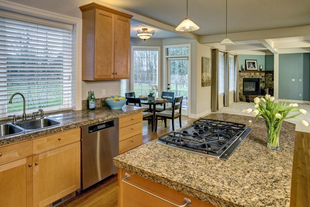 Foto på ett mellanstort amerikanskt kök, med en dubbel diskho, luckor med infälld panel, skåp i ljust trä, granitbänkskiva, flerfärgad stänkskydd, stänkskydd i sten, rostfria vitvaror, ljust trägolv och en köksö