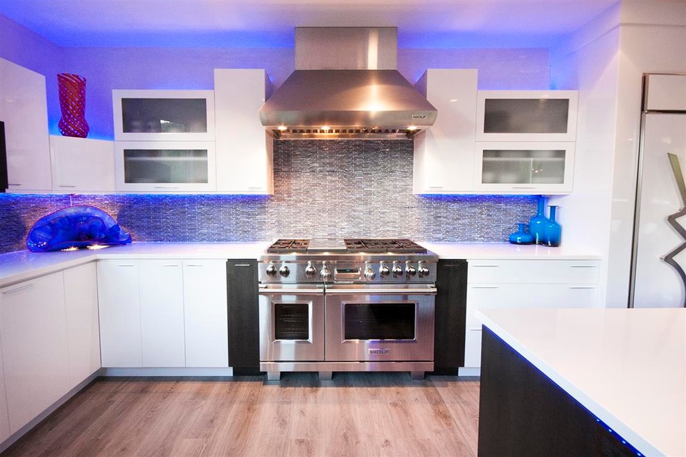Photo of a medium sized contemporary galley kitchen/diner in Denver with an integrated sink, flat-panel cabinets, white cabinets, engineered stone countertops, blue splashback, glass tiled splashback, integrated appliances, light hardwood flooring and an island.