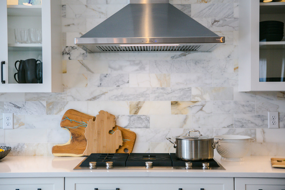 Cette image montre une grande cuisine américaine linéaire traditionnelle avec un évier encastré, un placard à porte shaker, des portes de placard blanches, un plan de travail en quartz modifié, une crédence multicolore, une crédence en marbre, un électroménager en acier inoxydable, un sol en bois brun, îlot, un sol marron et un plan de travail blanc.