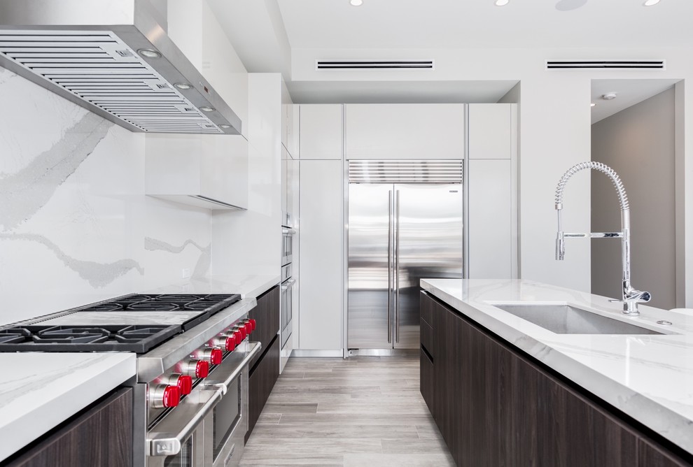 Example of a large minimalist l-shaped light wood floor and gray floor open concept kitchen design in Miami with an undermount sink, flat-panel cabinets, white cabinets, quartzite countertops, white backsplash, stone slab backsplash, stainless steel appliances and an island