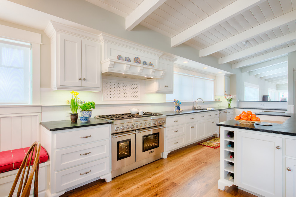 Klassisk inredning av ett kök, med luckor med infälld panel, vita skåp, rostfria vitvaror, mellanmörkt trägolv och en köksö