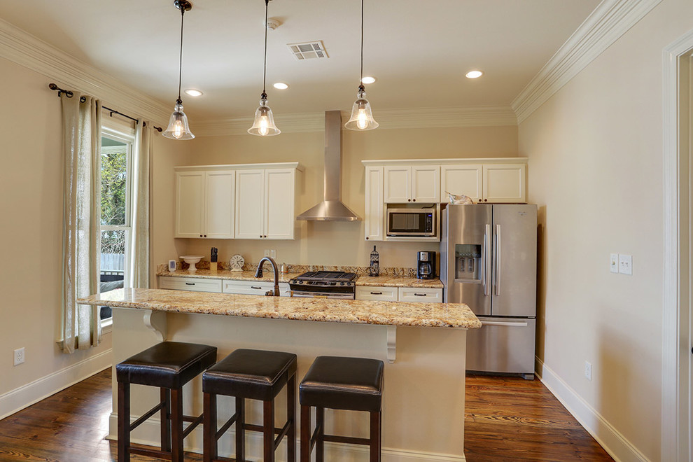 Large classic u-shaped enclosed kitchen in New Orleans with a built-in sink, flat-panel cabinets, white cabinets, granite worktops, stainless steel appliances, medium hardwood flooring, an island and brown floors.