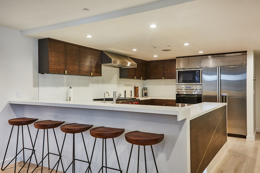 ロサンゼルスにある中くらいなコンテンポラリースタイルのおしゃれなキッチン (フラットパネル扉のキャビネット、濃色木目調キャビネット、珪岩カウンター、白いキッチンパネル、シルバーの調理設備、淡色無垢フローリング) の写真