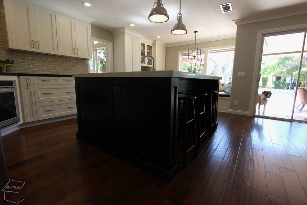 Large trendy l-shaped medium tone wood floor eat-in kitchen photo in Orange County with a drop-in sink, shaker cabinets, white cabinets, quartz countertops, beige backsplash, porcelain backsplash, stainless steel appliances and an island