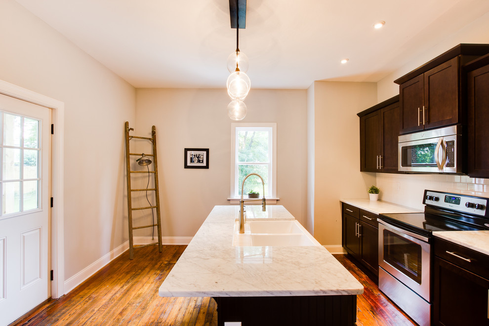 Inspiration for a mid-sized timeless single-wall medium tone wood floor enclosed kitchen remodel in Richmond with a farmhouse sink, shaker cabinets, dark wood cabinets, marble countertops, white backsplash, subway tile backsplash, stainless steel appliances and an island